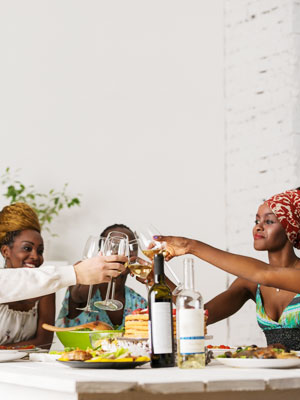 Südafrikanische Frauen und Männer prosten sich am gedeckten Tisch mit Weingläsern zu