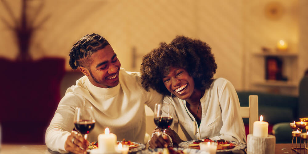Frau und Mann sitzen mit einem Glas Rotwein am gemütlichen Tisch und lachen fröhlich