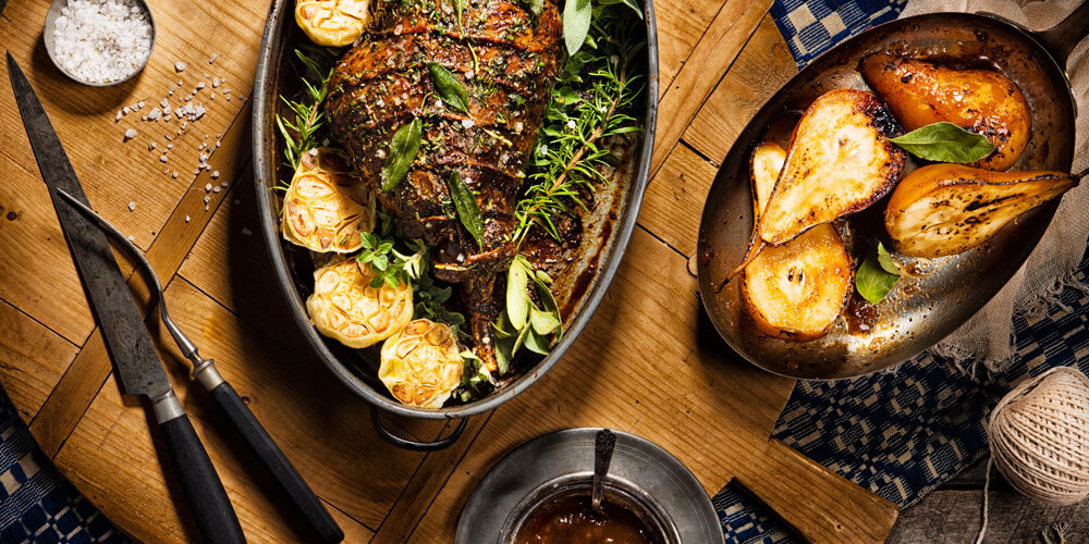 Traditionelles Osterlamm mit Beilagen, einladend angerichtet im Bräter auf einem rustikalen Holztisch