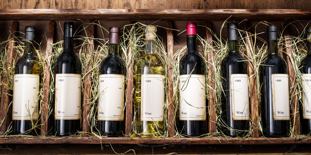 Weinflaschen liegen ordentlich sortiert nebeneinander in einer Weinkiste, die mit Bast ausgelegt ist