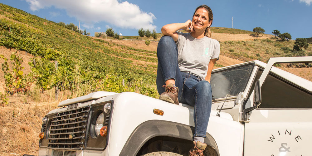 Sandra Tavares eine portugiesische Winzerin vom Weingut Wine & Soul sitzt lächelnd auf der Motorhaube Ihres Jeeps
