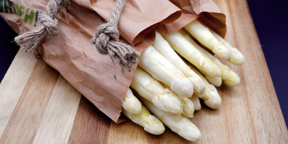 Frische weiße Spargelstangen in einer Papiertüte liegen auf einem Holztisch