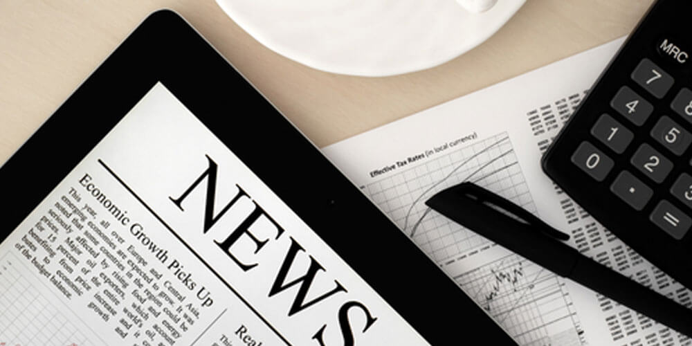 Digitales Tablet mit der Beschriftung News auf dem Display, neben einer Zeitung, Taschenrechner, Stift und Kaffeetasse