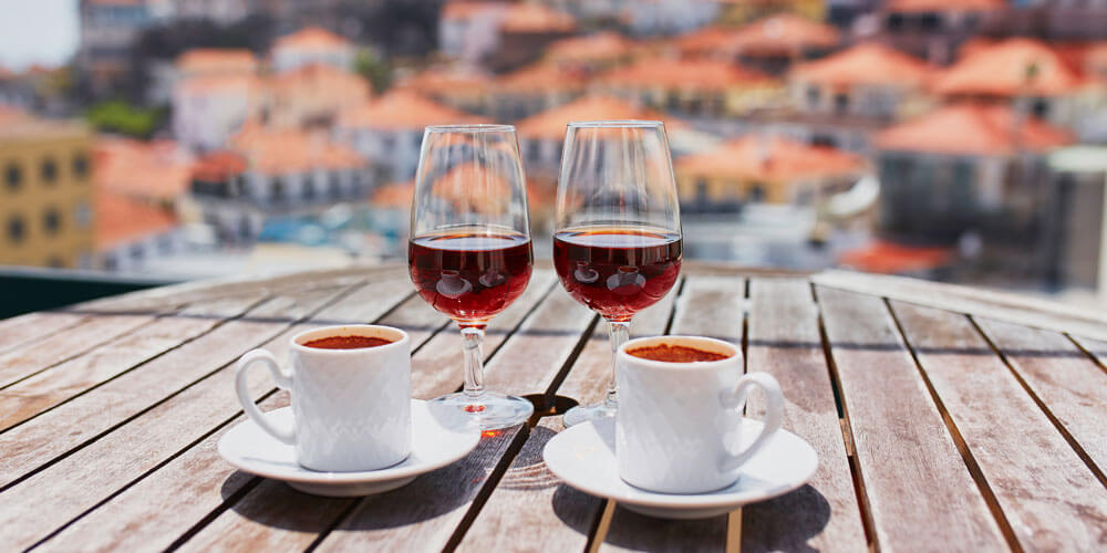 Blick über einen Tisch auf dem jeweils zwei mit Rotwein gefüllte Gläser und Espressotassen stehen