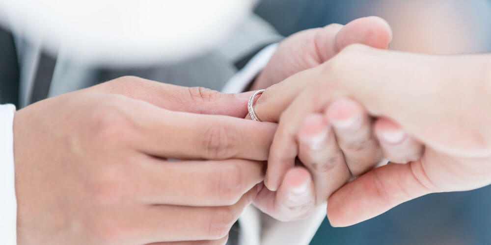 Männliche Hand steckt weiblicher Hand einen goldenen Ring an den Finger